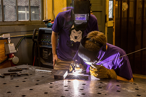 Two students with masks welding in a lab