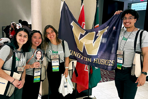 Four members of the SeaDawgs pose with the Washington Huskies flag