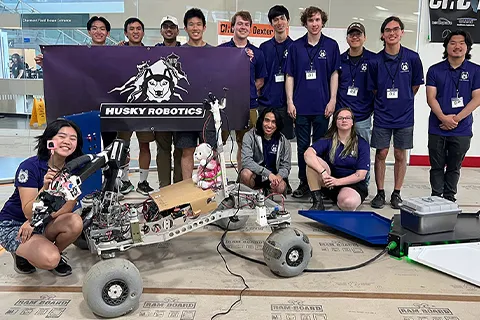 The Husky Robotics team wearing matching shirts, holding up a sign, and posing with their robot.