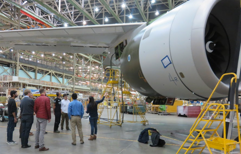 students standing below jet wing in Boeing plant