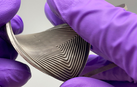 Close up of hands with purple gloves holding a small and stretchable generator that converts body heat to electricity.